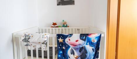A white crib with a blanket and a wall-mounted picture.