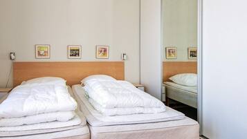 A hotel room with two single beds, a wooden headboard, and three framed pictures on the wall.