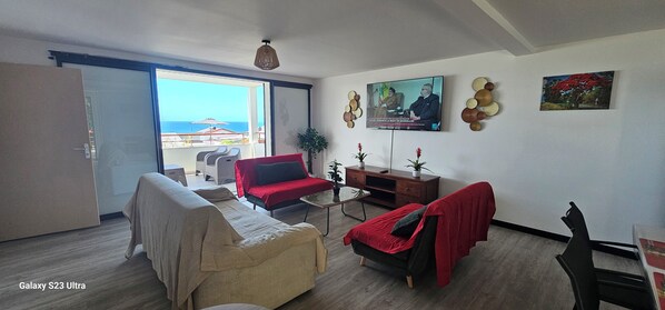 Ein modernes Wohnzimmer mit einer Couch, einem roten Sessel, einem kleinen Tisch und einem an der Wand befestigten Fernseher.