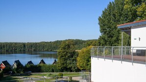 A wooden deck with a view of a lake and houses in the background. - Apartment fur den Perfekten Urlaub (Mirow)