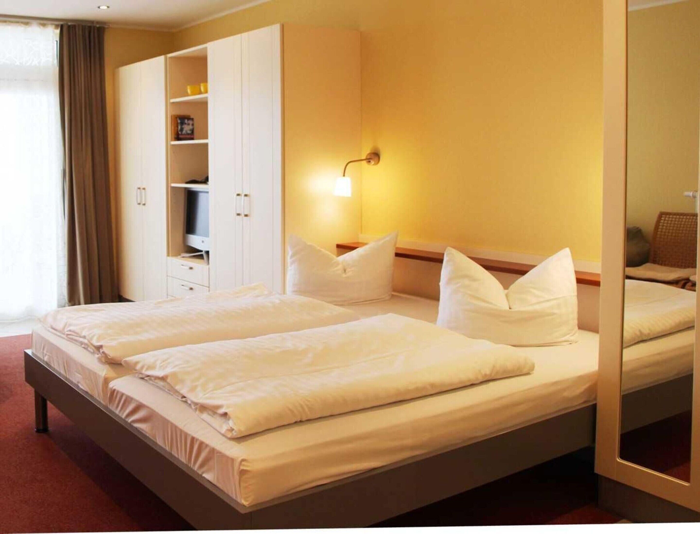 A hotel room with a large bed, a wardrobe, a bedside table, and a mirror.