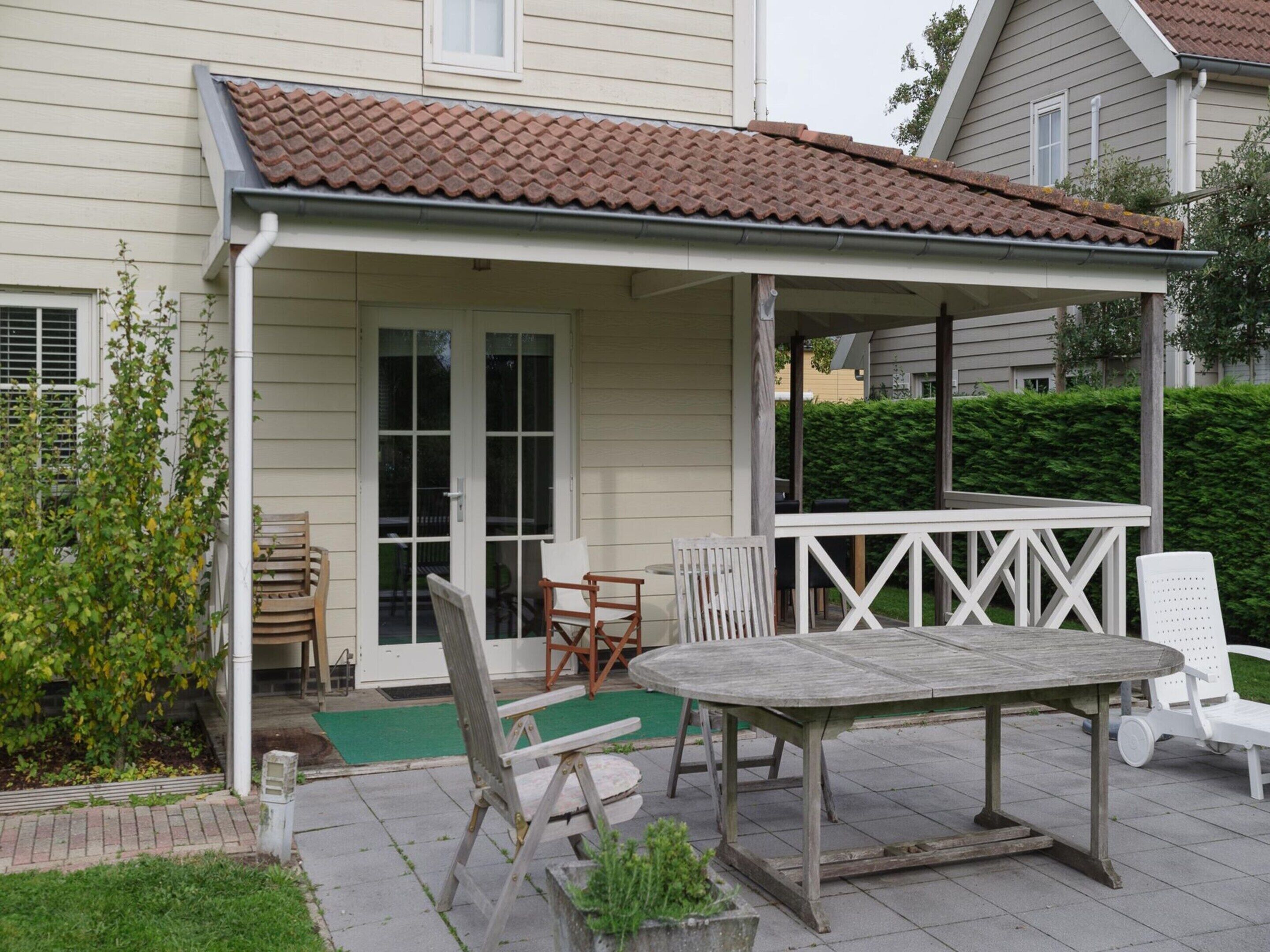 A covered patio with a table and chairs, a small garden area, and a house with a tiled roof and white siding.