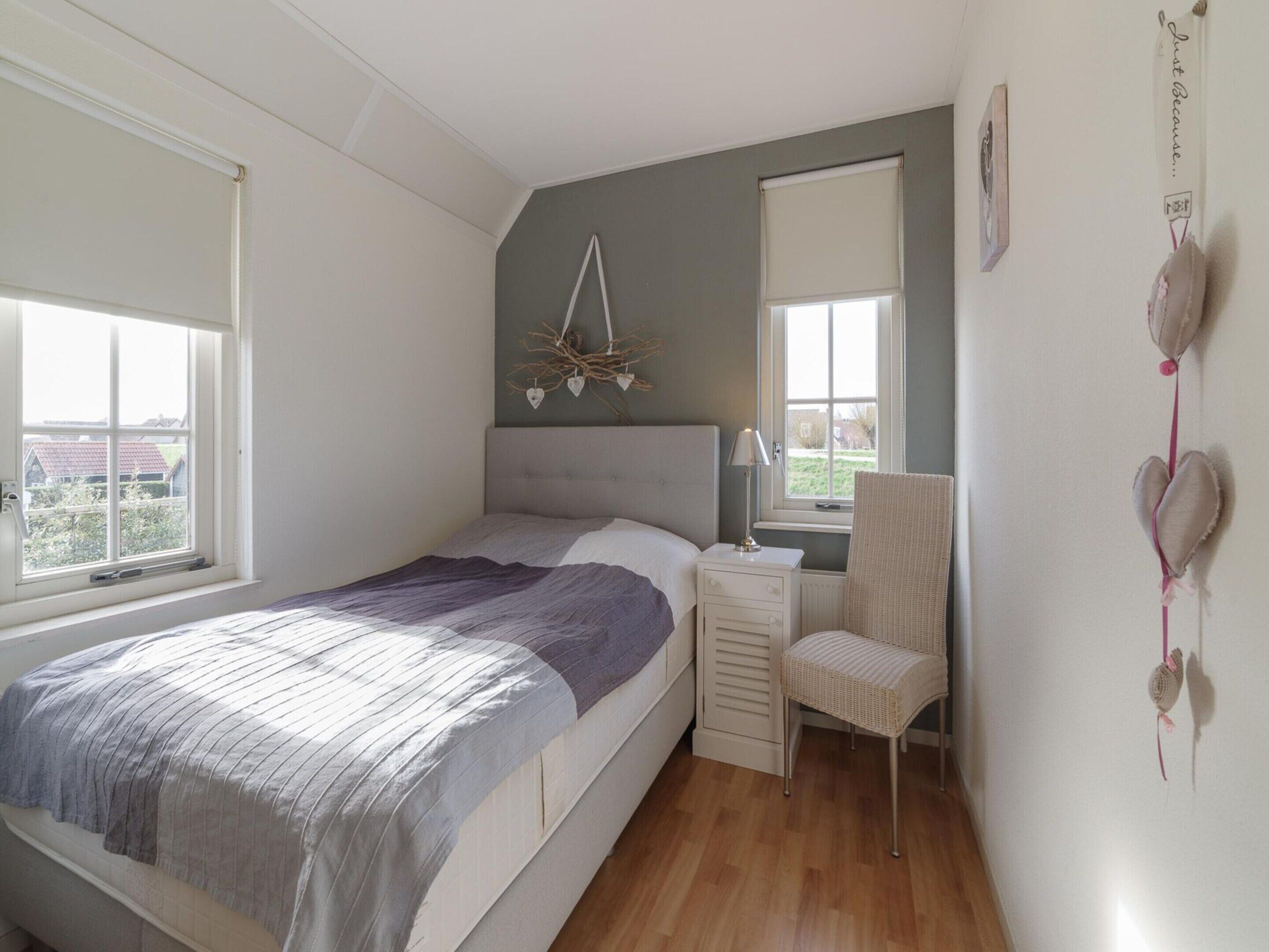 A bedroom with a bed, bedside table, chair, and a window.