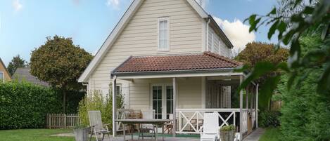 A two-story house with a covered porch, a small garden, and outdoor seating.