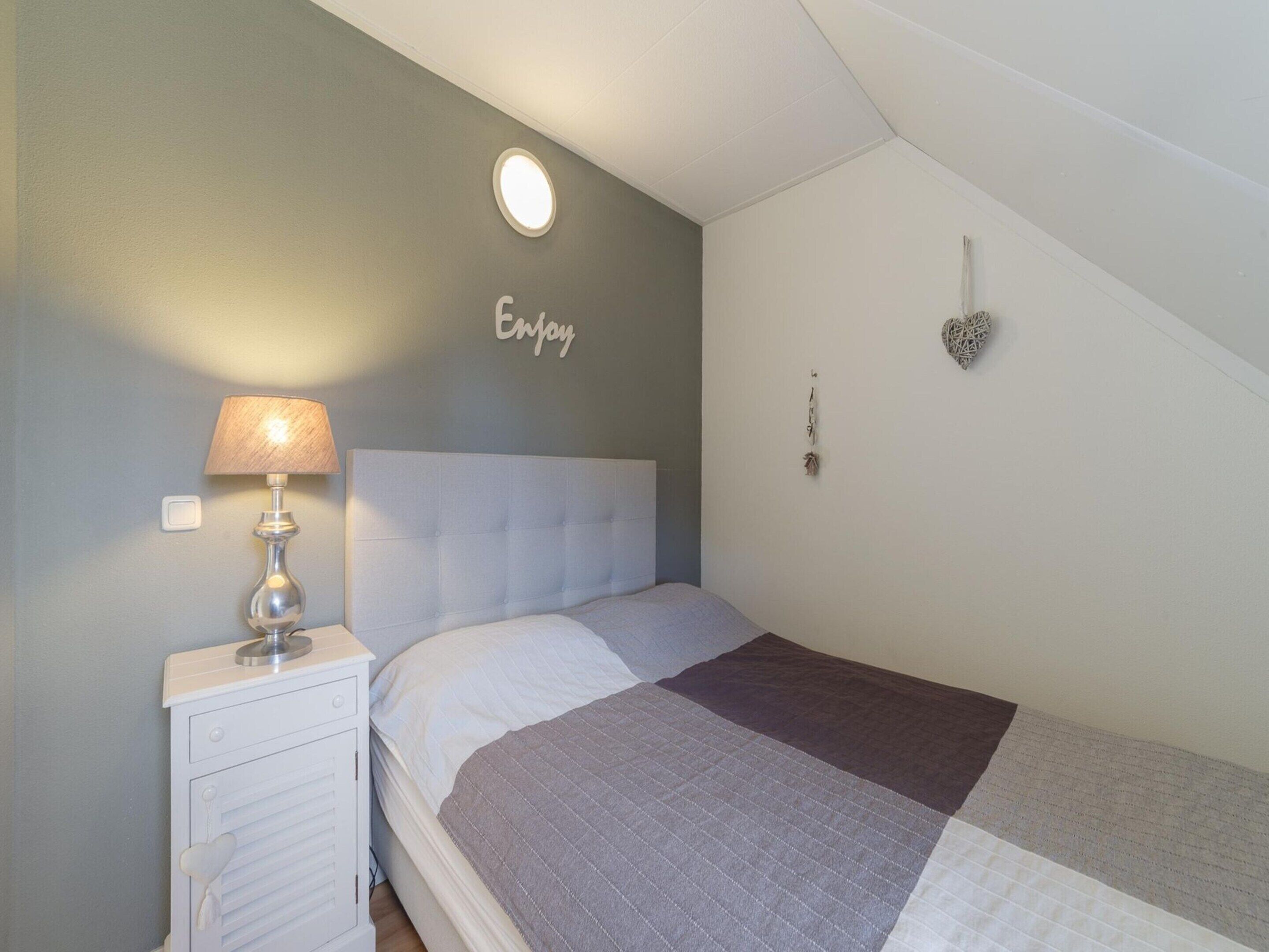 A bedroom with a bed, a nightstand, a lamp, a wall-mounted light, and decorative items.