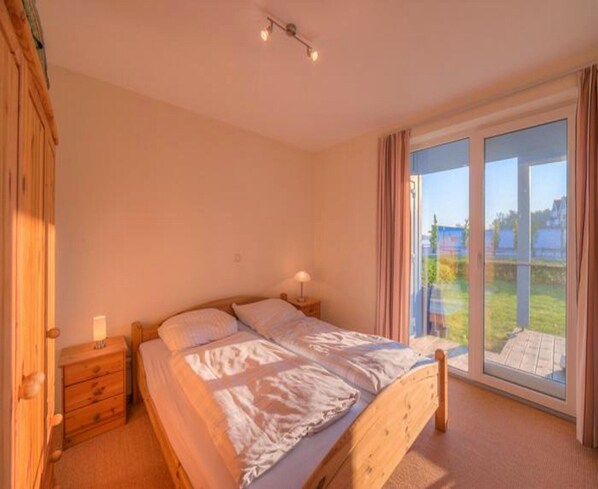 Une chambre à coucher avec un lit, des tables de chevet, une lampe et une grande fenêtre donnant sur l’extérieur.