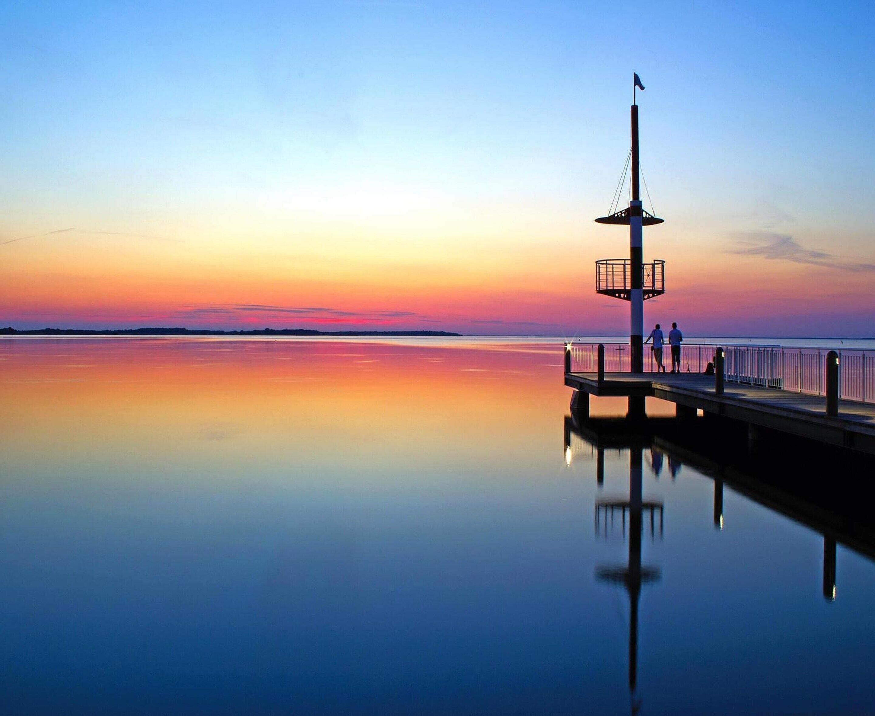 A pier extending into calm waters with a clear sky at sunset.