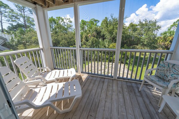 A covered outdoor deck with white plastic chairs and a patterned cushion.