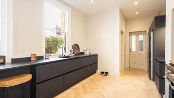 A modern kitchen with black cabinetry, a wooden herringbone floor, a large window, and a door leading to another room.