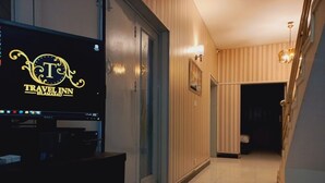 Un pasillo con un televisor mostrando el logotipo de Travel Inn Islamabad, una puerta y una escalera.