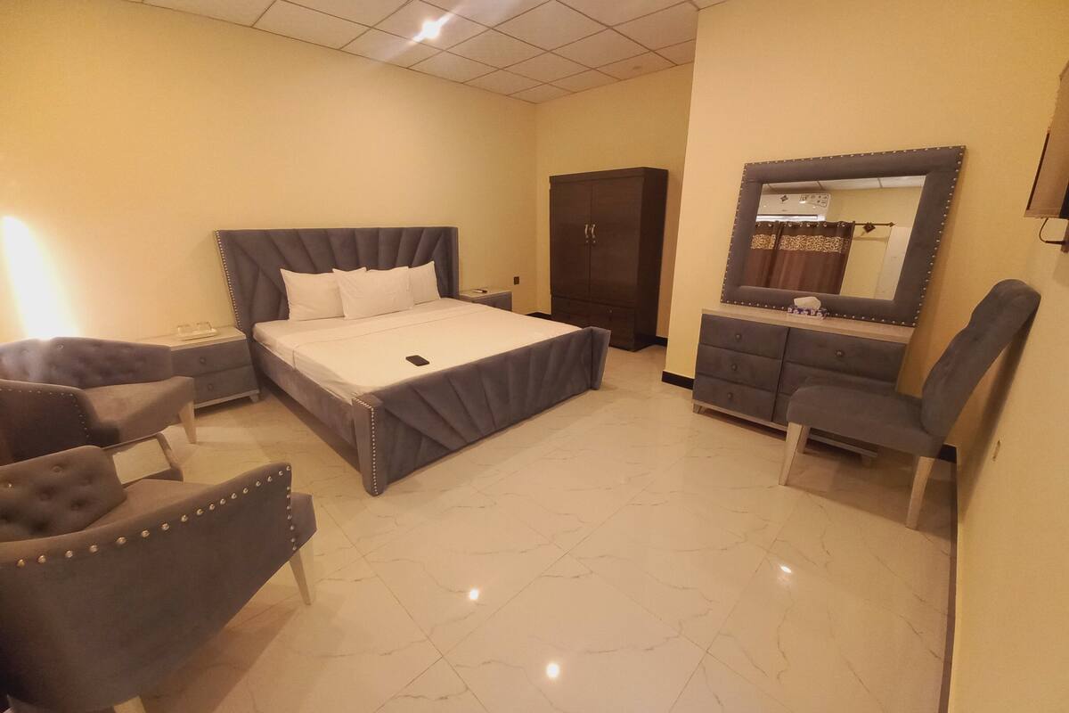 A bedroom with a bed, a wardrobe, a vanity with a mirror, and two armchairs.