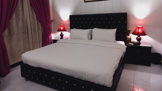 Una habitación de hotel con una cama, dos mesitas de noche con lámparas, un cuadro en la pared y una ventana con cortinas.