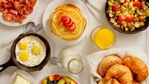 Una mesa con desayuno que incluye panqueques, huevos, tocino, cruasanes y fruta.