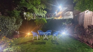 Un jardín cuidado con césped, dos sillas azules y plantas en macetas.