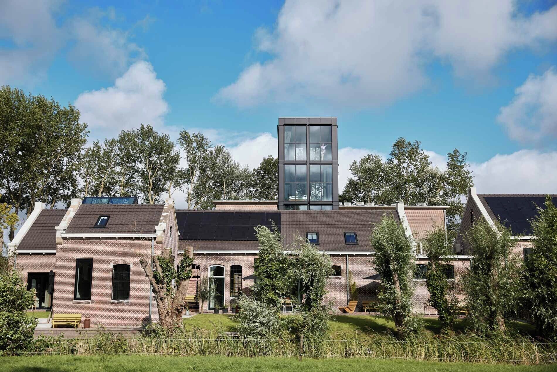 A modern building with a prominent glass tower, brick walls, and a well-maintained garden.