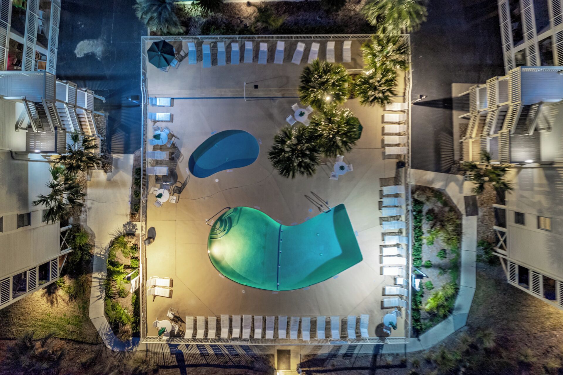Luftaufnahme eines Hotelinnenhofs mit mehreren Schwimmbecken, Liegebereichen und dichter Bepflanzung.