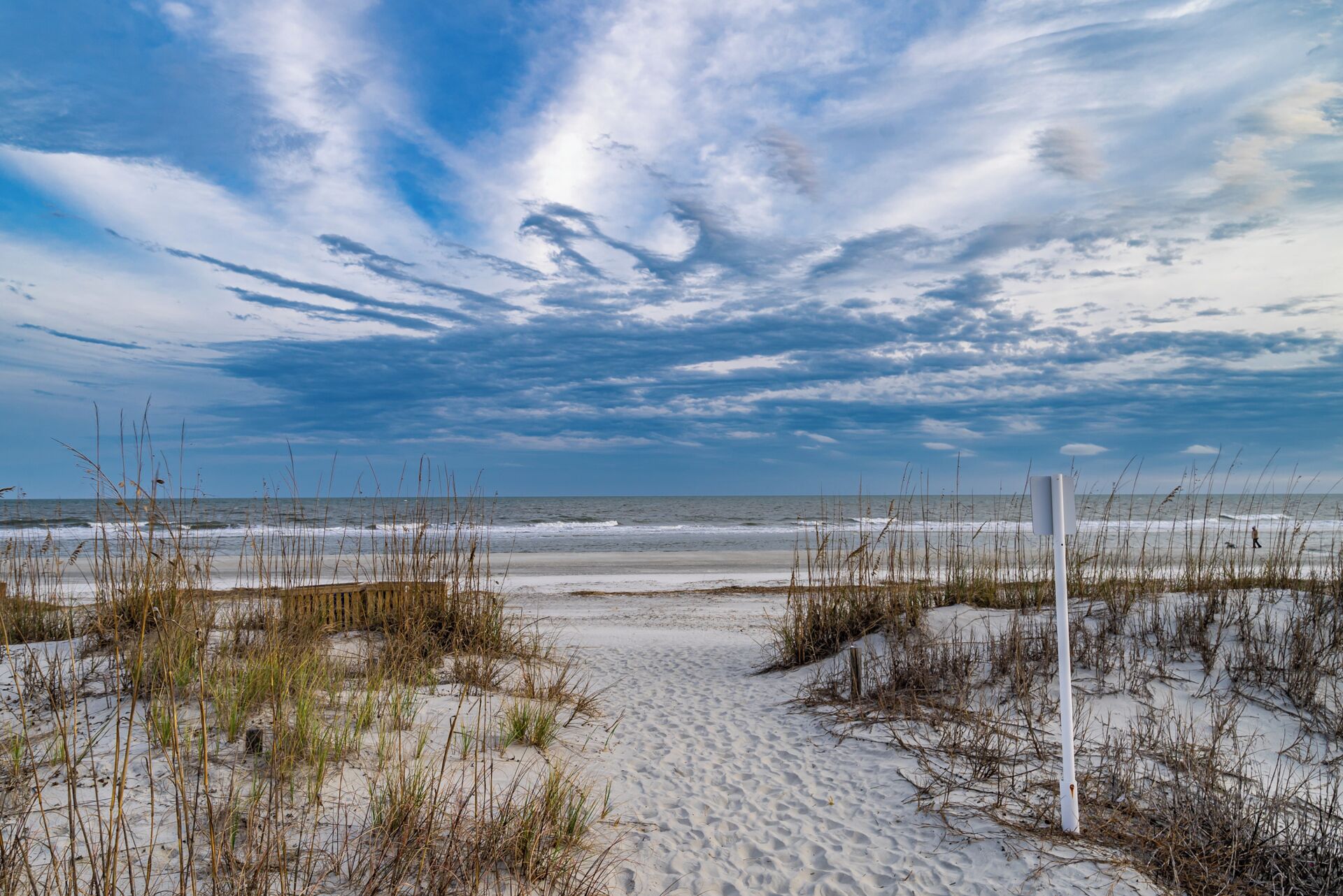 A sandy beach with sparse vegetation and a white post in the foreground.