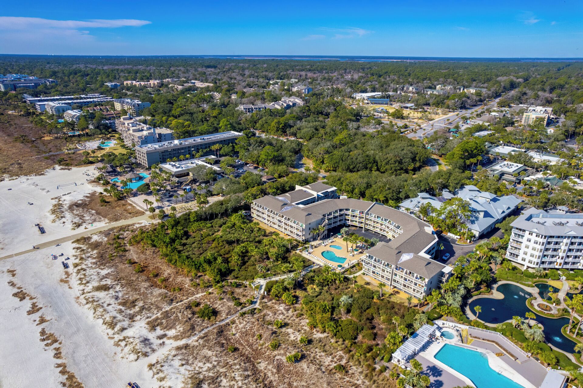 An aerial view of a resort with multiple buildings, a large pool, and surrounding greenery.
