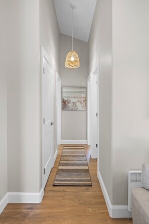 A hallway with a wooden floor, white walls, and a hanging pendant light.