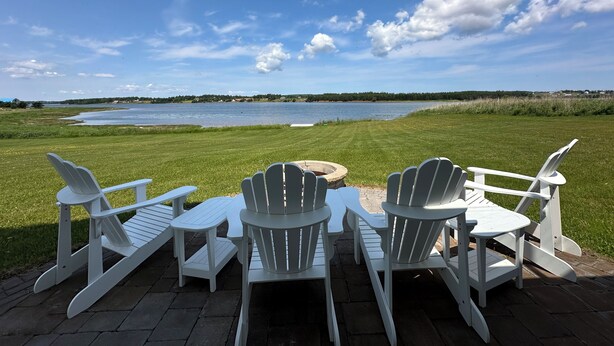 Een terras met witte Adirondack-stoelen en een vuurkuil van steen, met uitzicht op een meer.