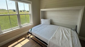 Een slaapkamer met een bed, een groot raam en uitzicht op een groen veld.