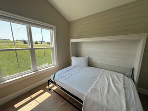 A bedroom with a bed, a large window, and a view of a green field.