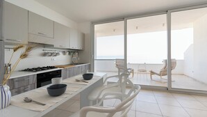 Eine moderne Küche mit Essbereich, große Schiebeglasfenster zu einem Balkon mit Meerblick.