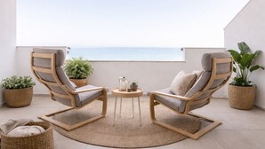 Ein Balkon mit zwei Holzstühlen, einem kleinen runden Tisch und Blumentöpfen.