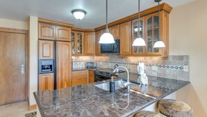 Una cocina con gabinetes de madera, encimera de granito, microondas integrado e iluminación colgante.