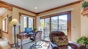 Una habitación con escritorio, computadora, sillón de cuero y vistas a las montañas a través de amplios ventanales.