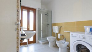 Ein Badezimmer mit Dusche, Toilette, Bidet, Waschbecken und Waschmaschine.