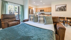 A bedroom with a bed, two brown leather chairs, a dining table, a kitchen area with cabinets and appliances, and a large window with curtains. - 2 Mi to Dtwn Flagstaff: Home w/ Balcony! (Flagstaff)
