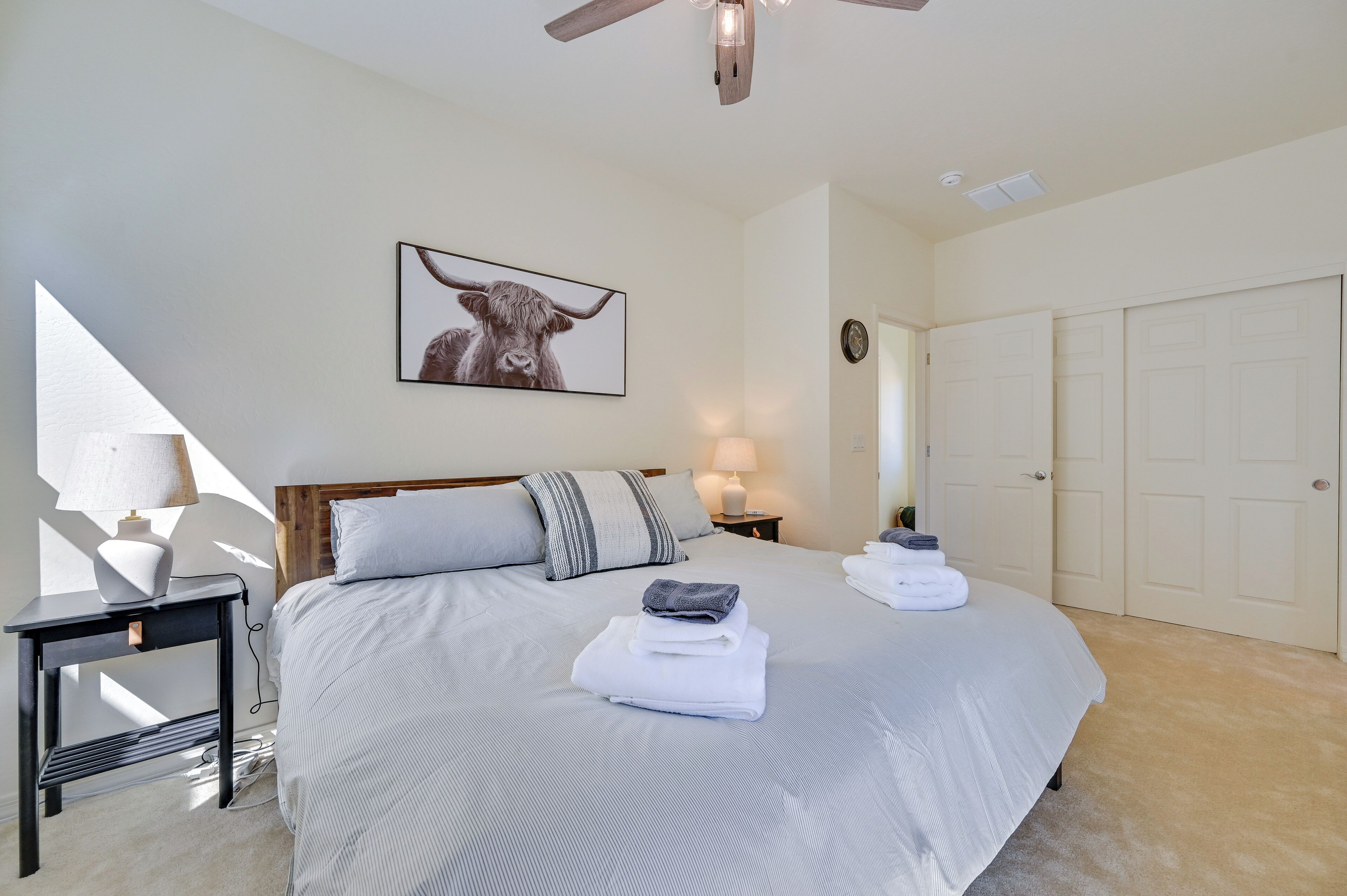 A bedroom with a bed, a nightstand, a lamp, a ceiling fan, a framed picture, and a closet.