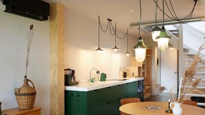 A modern kitchen with green cabinets, a wooden dining table, and pendant lights. - Suvelfabryk appartement 10 (Ljussens)