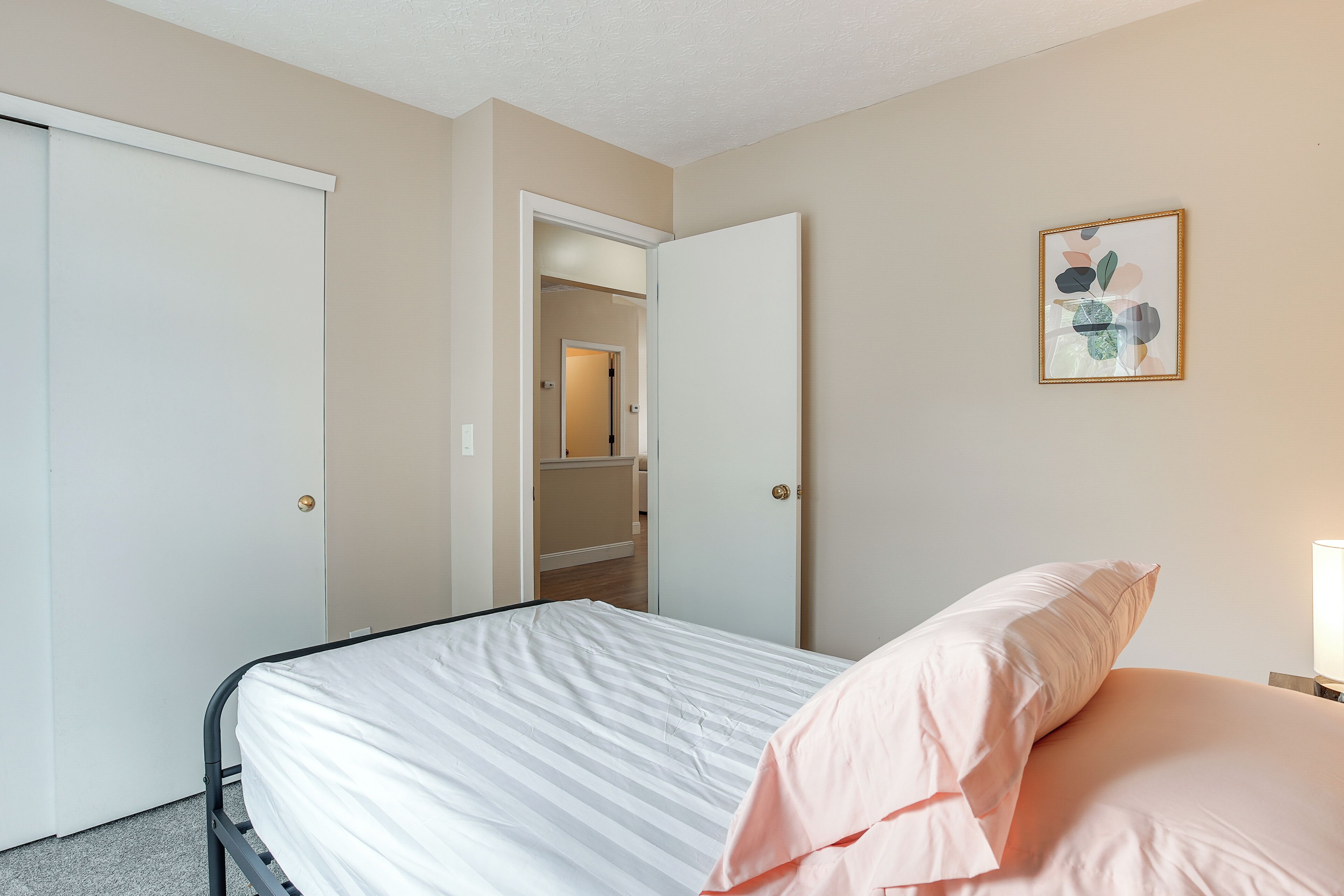 A bedroom with a bed, a door, and a wall-mounted picture.