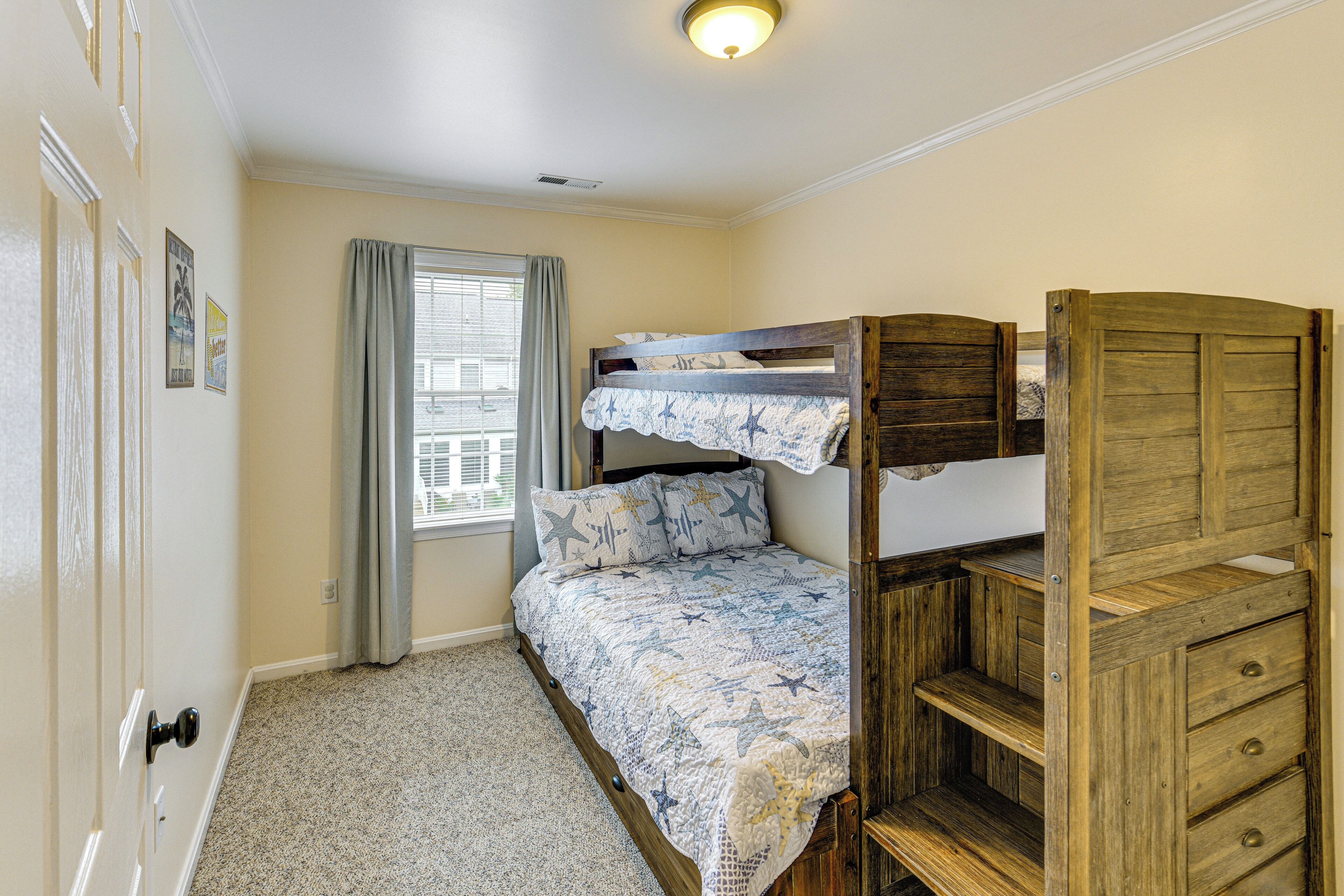 A bunk bed with a star-patterned bedspread, a window with curtains, and a wooden dresser with drawers.