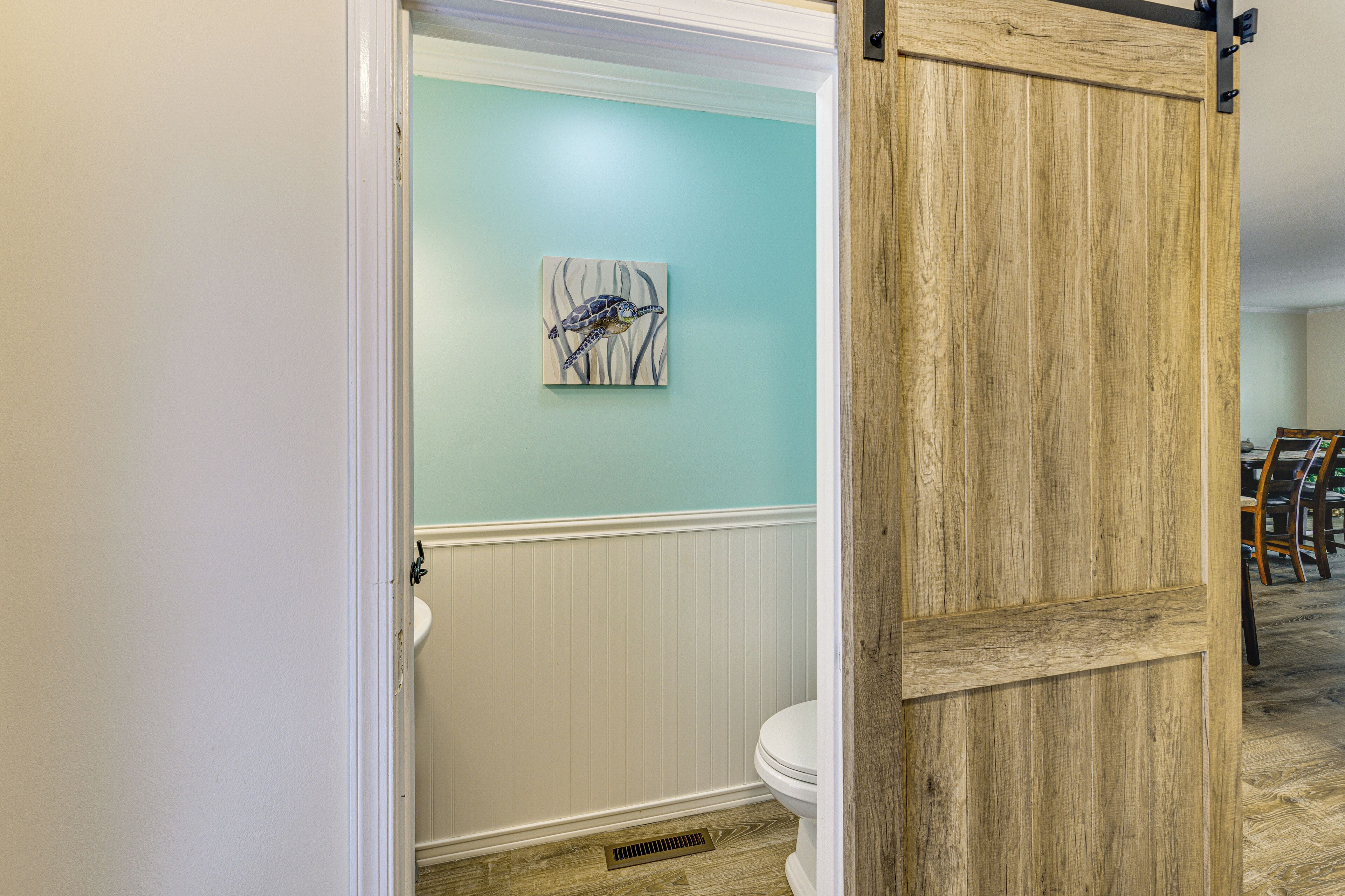 Un baño con inodoro blanco, pared de azul claro y puerta de madera.