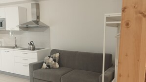 Una cocina moderna con armarios blancos, un sofá gris y una tetera sobre la encimera.