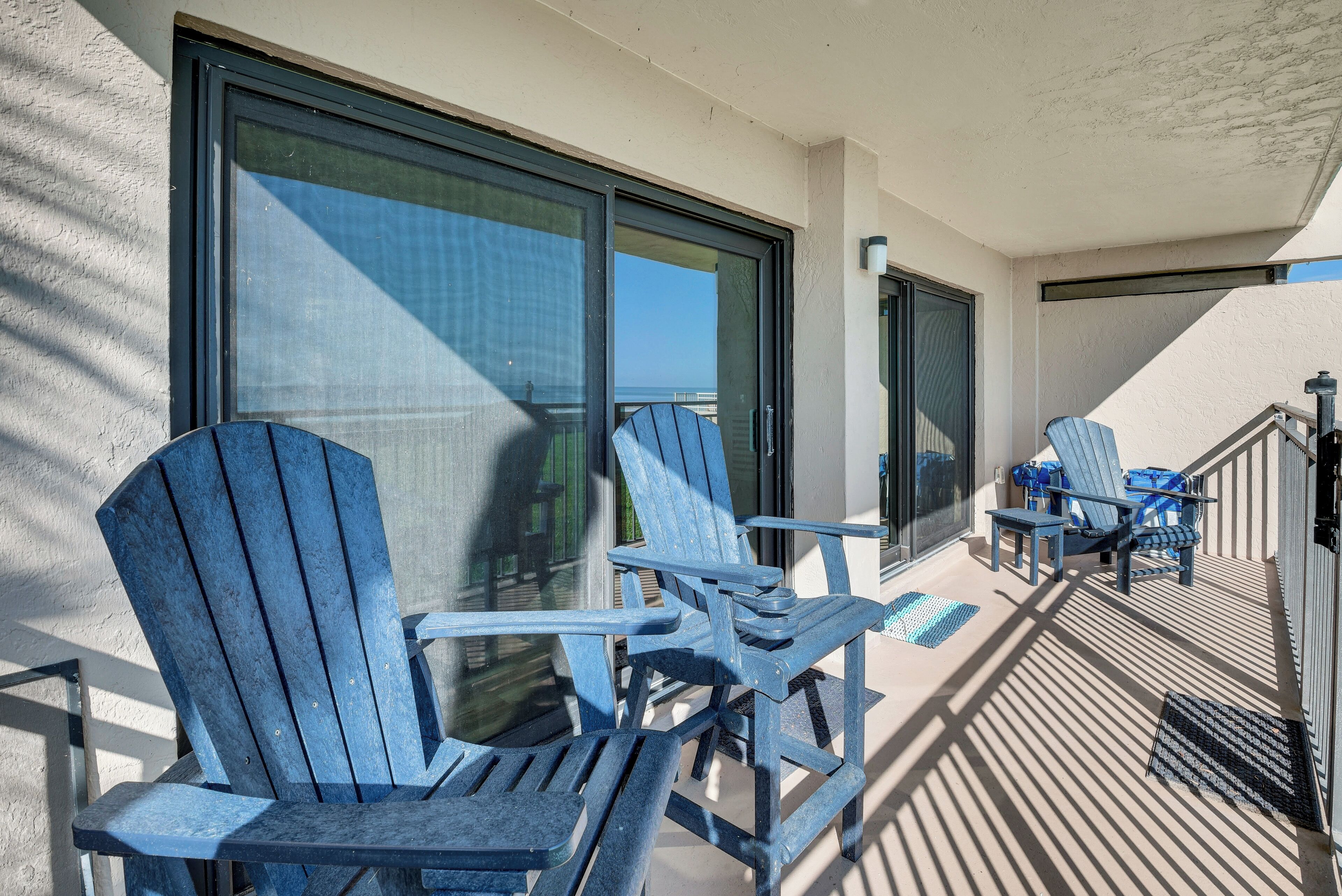 Un balcon avec deux fauteuils Adirondack, une petite table et une vue sur l’océan.