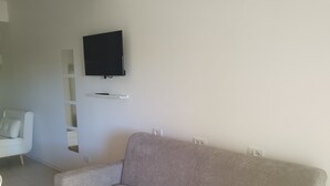 Un salon avec un canapé gris, un téléviseur à écran plat fixé au mur et un fauteuil blanc.