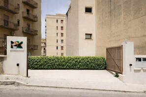 Ein begrenzter Wohnbereich mit einer Hecke, einem Schild mit geometrischem Design und einem hohen Gebäude im Hintergrund.