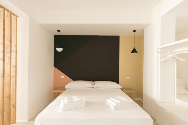 Ein modernes Hotelzimmer mit einem Bett, Nachttischen, einer Hängelampe und einem Kleiderschrank.