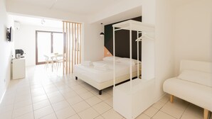 Une chambre moderne avec un lit à baldaquin blanc, un canapé blanc et un coin repas comprenant une table et des chaises.