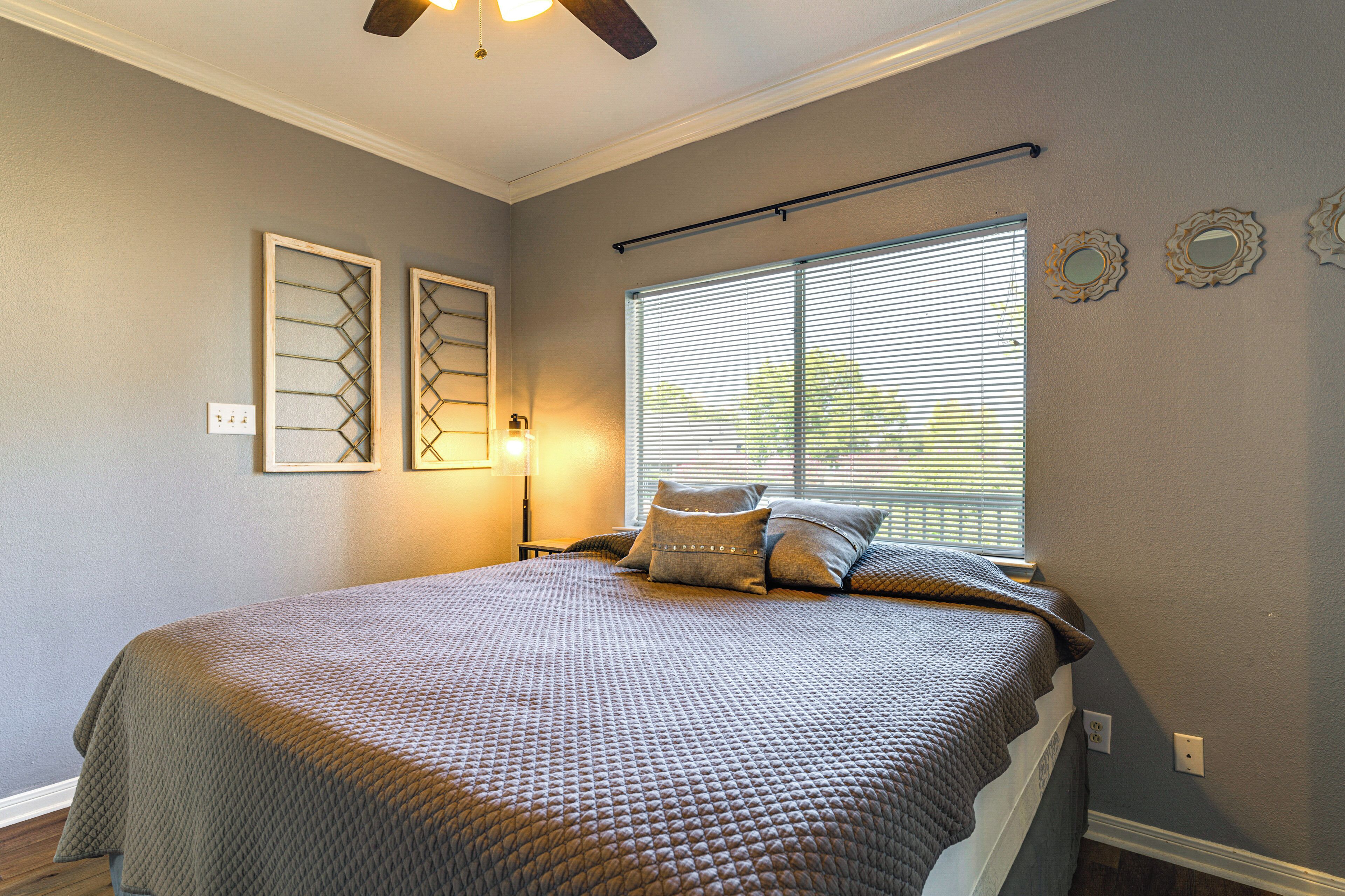 A bedroom with a large bed, a window with blinds, a ceiling fan, and wall-mounted decor.