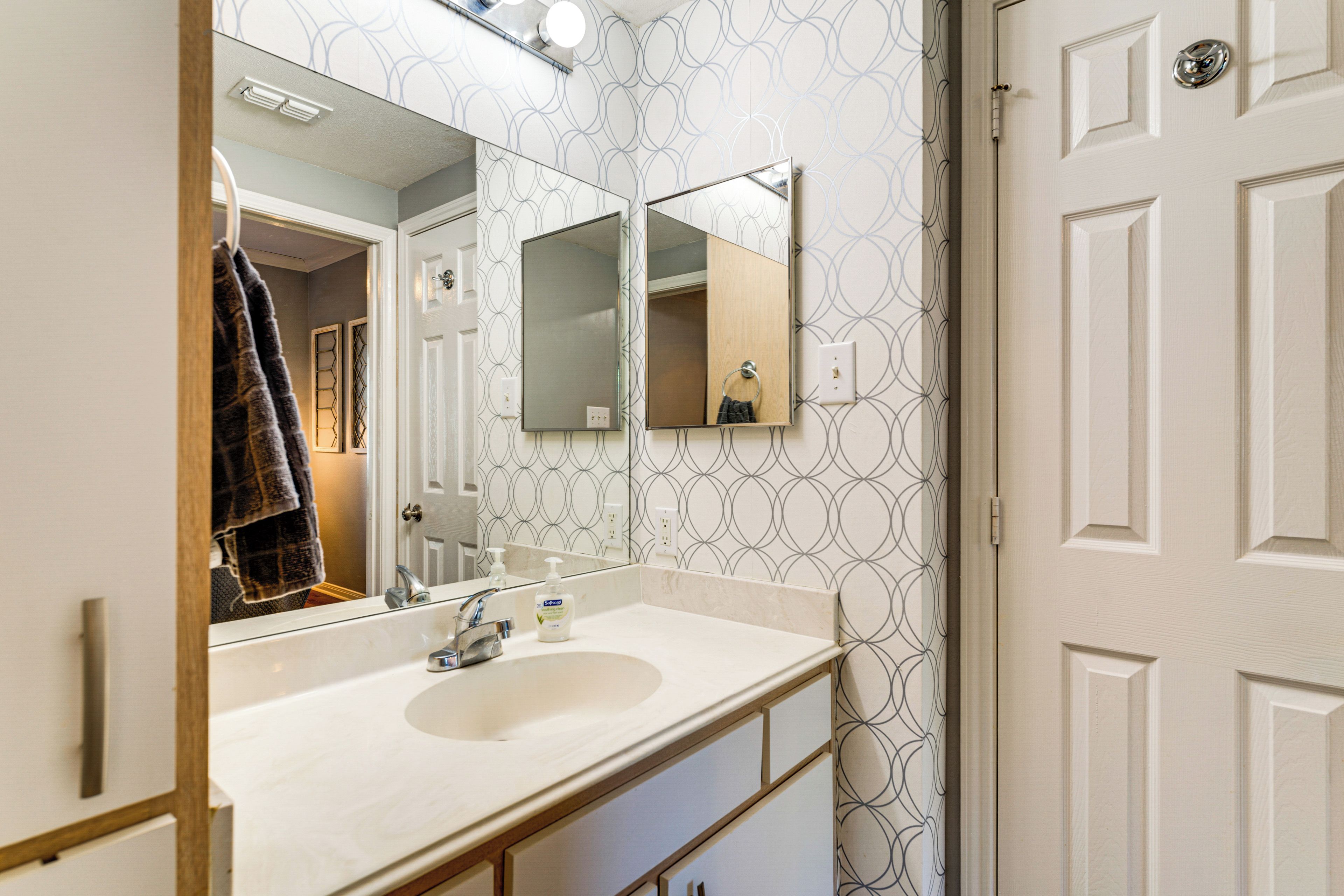 A bathroom with a white sink, two mirrors, and patterned wallpaper.