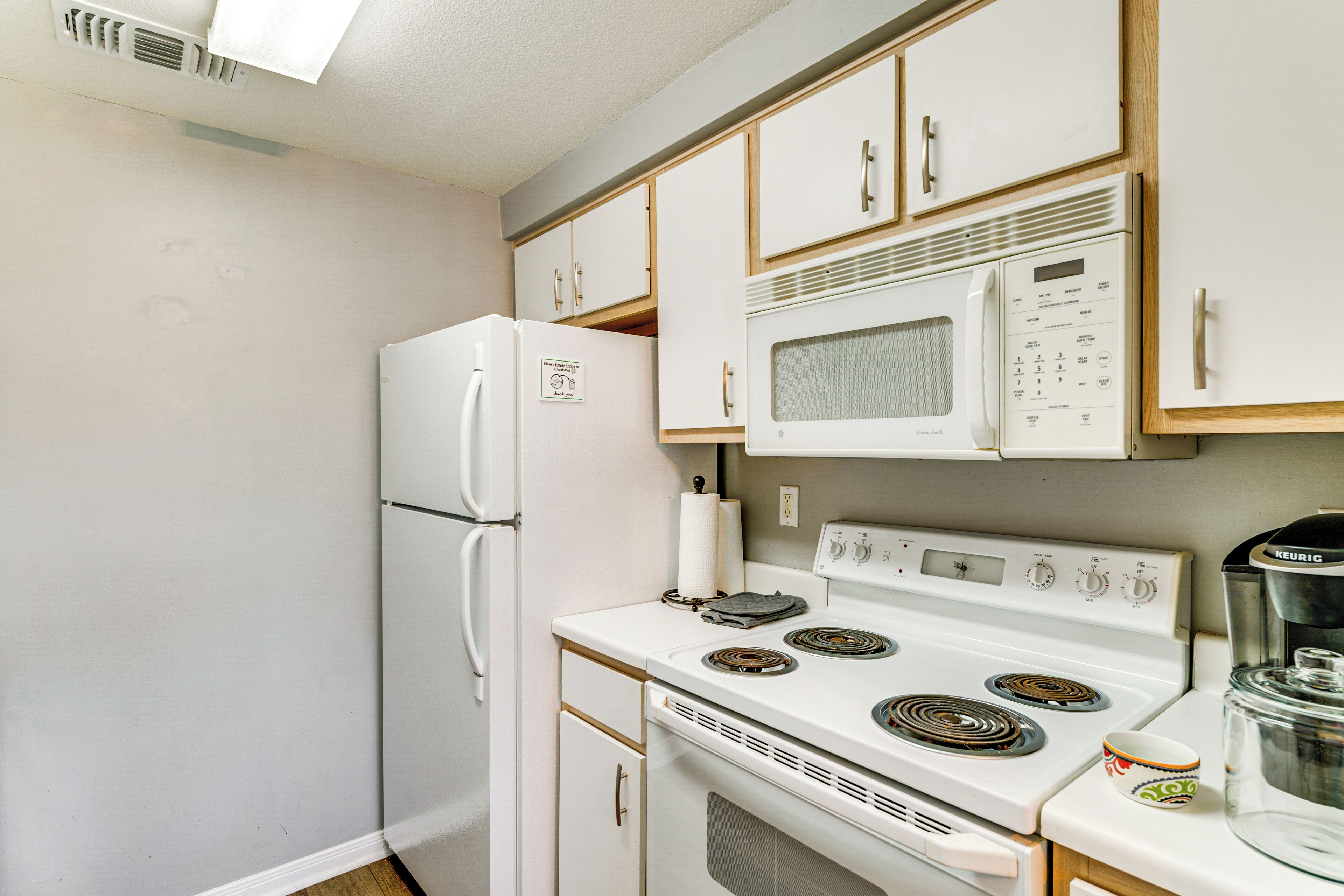 A compact kitchen with white appliances, including a refrigerator, microwave, and stove, with wooden cabinets and a coffee maker.