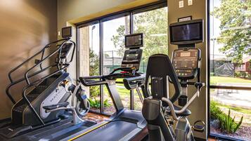 A fitness center with treadmills, stationary bikes, and a rowing machine, equipped with heart rate monitors and a TV screen.