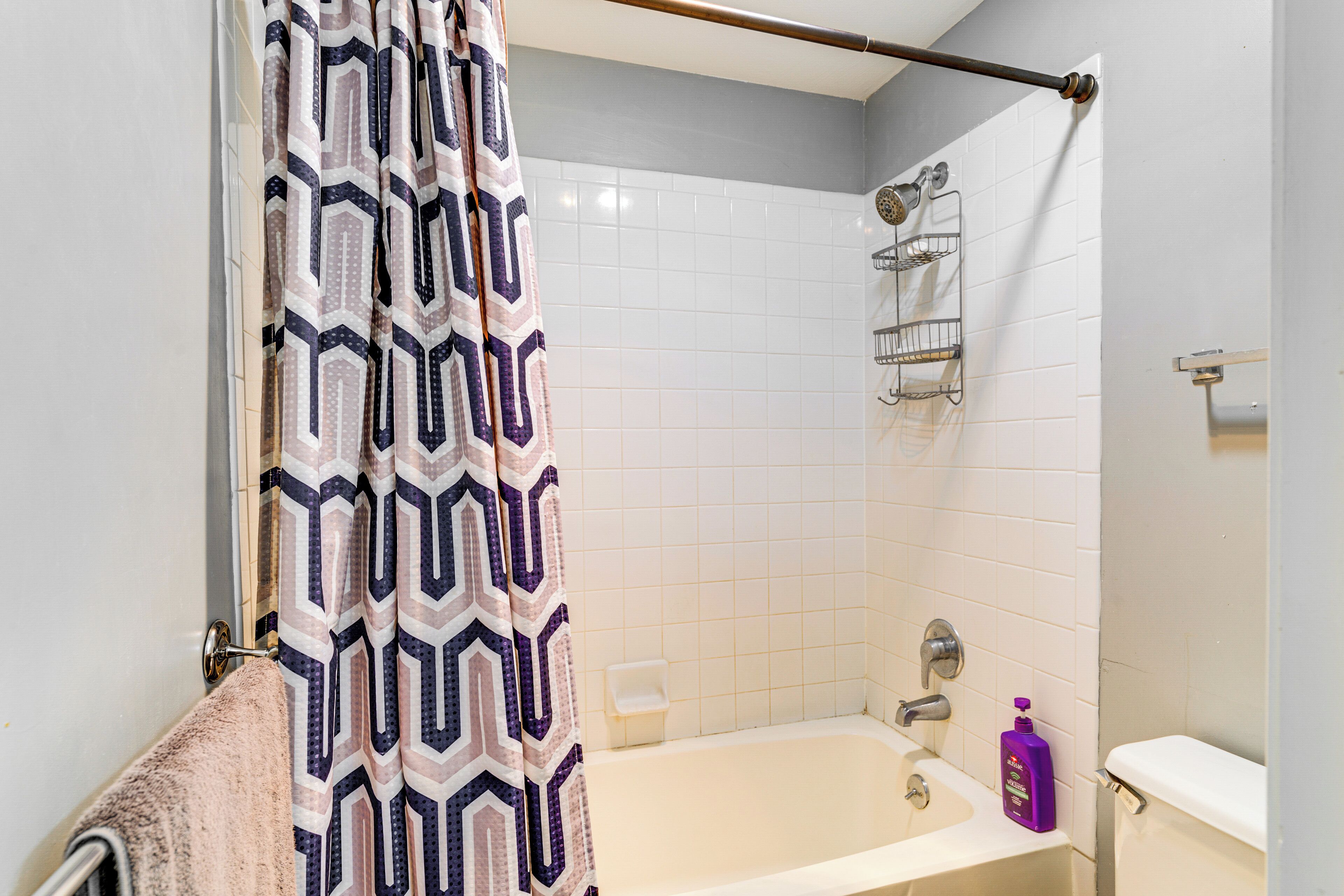 A bathroom with a shower curtain, a bathtub, a toilet, and a soap dispenser.
