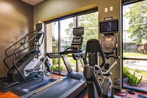 Un gimnasio con cintas de correr, bicicletas estáticas y una máquina de remo, equipado con monitores de frecuencia cardíaca y una pantalla de televisión.