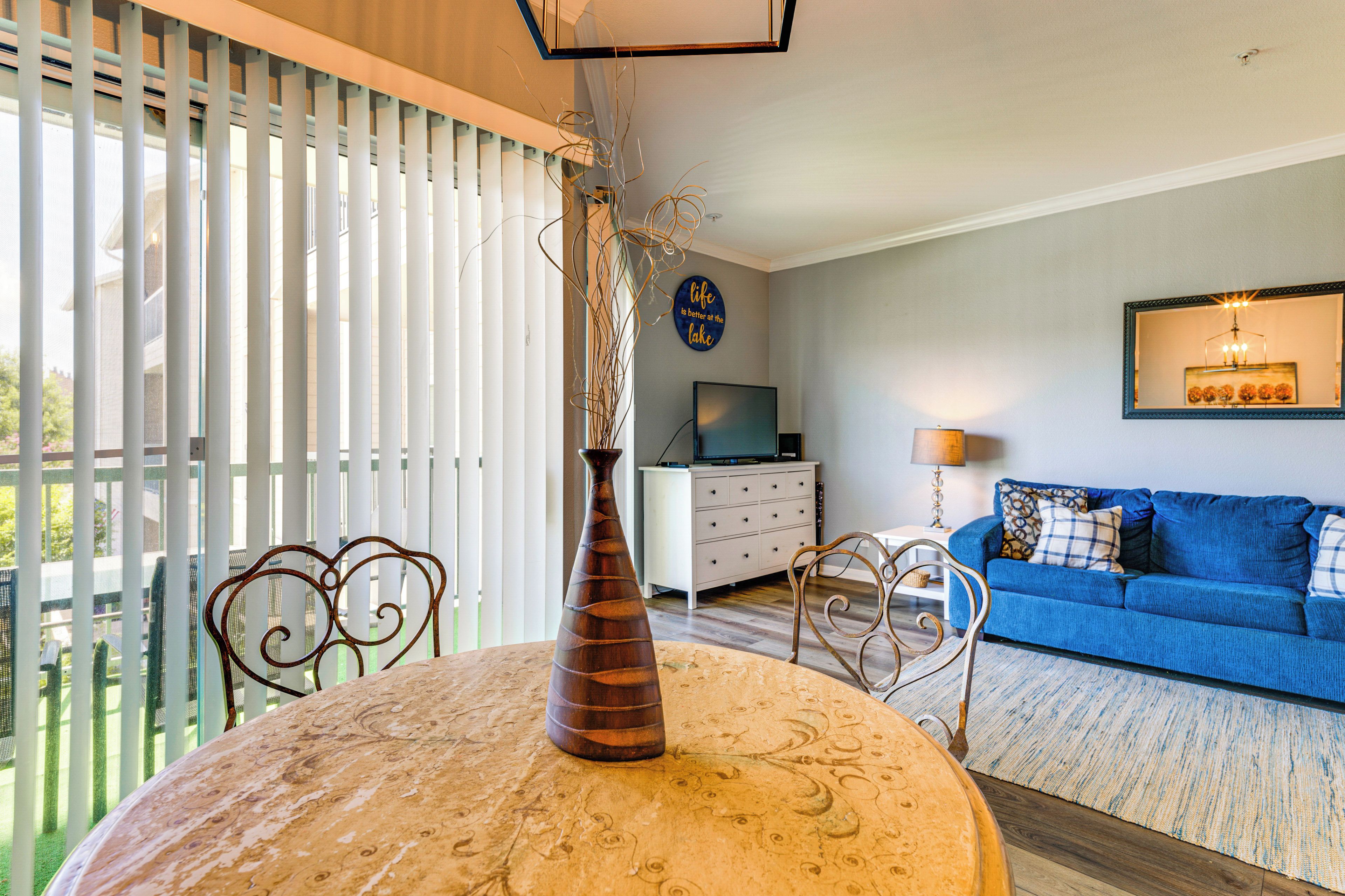 Una sala de estar con un sofá azul, un aparador blanco, un televisor y una mesa de comedor con un jarrón.